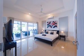 A modern hotel room with a large bed, a ceiling fan, a TV, and a balcony with outdoor furniture.