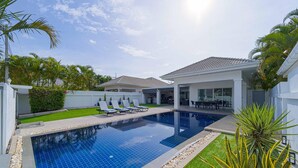 A swimming pool with lounge chairs, a covered patio, and a house with a tiled roof. - Cozy 3 Bedroom Pool Villa L70 (Hua Hin)