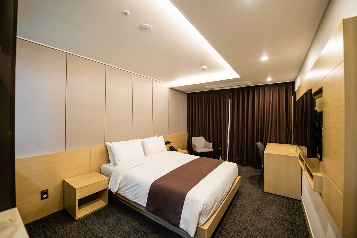 Una habitación de hotel moderna con una cama grande, un escritorio, una silla y un televisor.