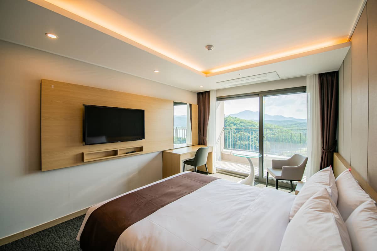 Habitación de hotel moderna con una cama grande, un televisor de pantalla plana en la pared, un escritorio con silla y un balcón con vistas a las montañas.