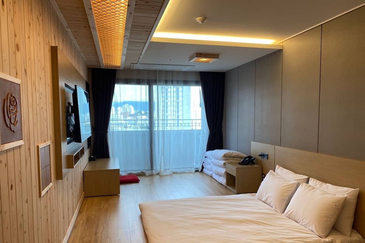 Habitación de hotel con cama, televisor, mesita de noche y ventana con cortinas.