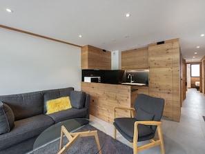 A modern living room with a grey sofa, a wooden chair, and a glass coffee table.