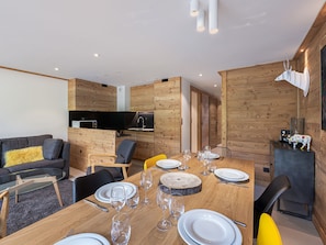 A modern interior with a wooden dining table set for four, a sofa, and a kitchen area.