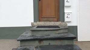 Una porta d'ingresso con una targa con il numero '4', un piccolo portico con gradini in pietra e un'anta di garage bianca a destra.