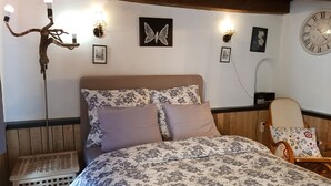 Camera da letto con copripiumino floreale, testiera e pavimento in legno, una sedia di legno e una sveglia a parete.