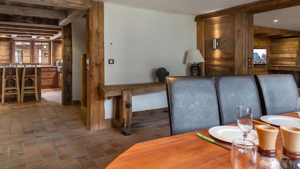 Comedor de madera con un banco y sillas, una mesa dispuesta para dos personas con platos, vasos y cubiertos.