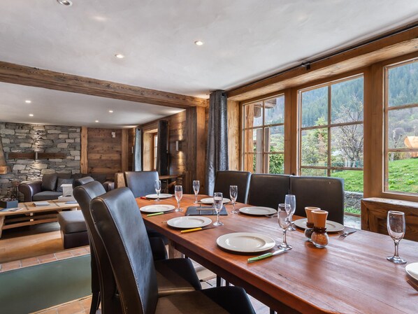 A dining area with a long wooden table set for six, surrounded by leather chairs.