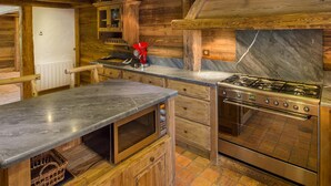 Una cocina rústica con vigas de madera, estufa a gas, microondas y una tetera roja.