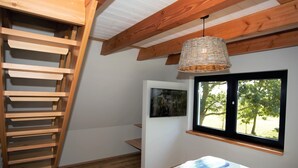 Un dormitorio con una escalera de madera, una cama con una colcha azul, un cuadro en la pared y una ventana con vistas a árboles.