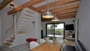 Una cocina moderna con un ventanal grande, un comedor con mesa y sillas de madera, y una escalera que sube a otro nivel.