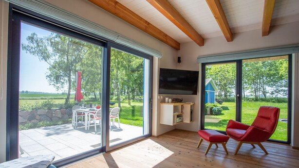 Una sala de estar moderna con grandes puertas correderas de vidrio, techo de madera y una silla roja.
