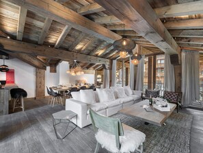 Un vaste espace de vie doté d’un haut plafond en bois, d’un canapé blanc, d’une table à manger et d’un fauteuil vert agrémenté d’un plaid en fausse fourrure blanche.
