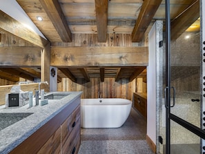 Une salle de bain dotée d’une baignoire îlot, de poutres en bois, d’un comptoir en granit et d’une cabine de douche en verre.