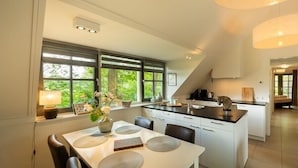 Une cuisine moderne dotée d’un îlot central, de grandes fenêtres et d’un coin repas avec une table dressée pour quatre personnes.