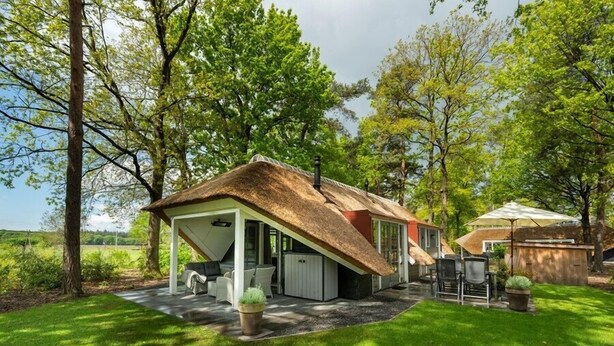 Une maison avec un toit en pente, un patio couvert et un espace jardin aménagé avec des sièges.