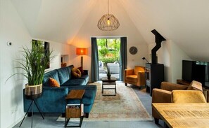 Relax in this stylish living room with a high ceiling, featuring a dark sofa, armchair, and coffee table, and a balcony with a serene view.