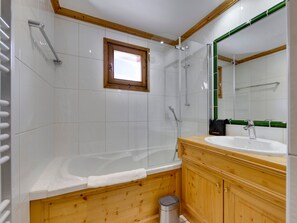 A bathroom with a wooden vanity, a bathtub, a shower enclosure, and a window.