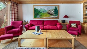 Un salon chaleureux avec un plafond en bois, un canapé rouge, une table basse en bois et un tableau représentant un paysage de montagne.