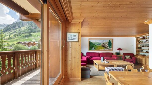 Un intérieur en bois avec un balcon, un canapé rouge, une table en bois et un tableau accroché au mur.