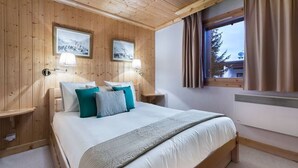 Une chambre à coucher aux murs lambrissés, avec un lit, deux tables de chevet et une fenêtre avec des rideaux.