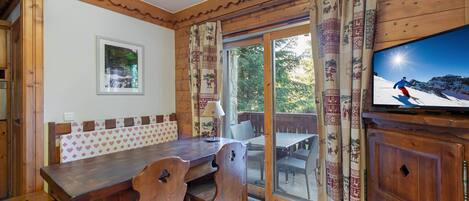 Un comedor de madera con una mesa y sillas, un televisor sobre un mueble de madera, y un vidrio corredero que da a un patio exterior.
