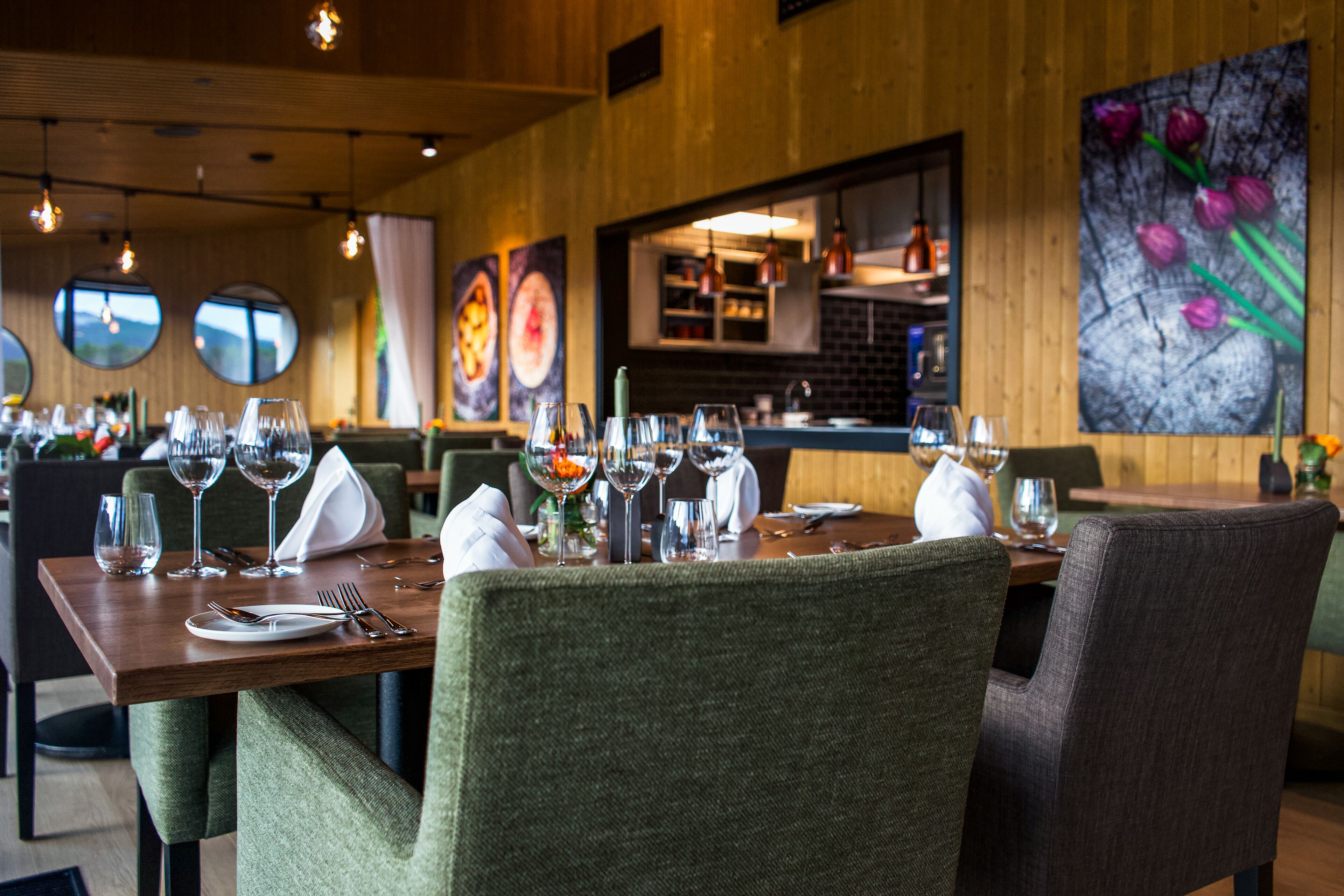 Een restaurant met ronde ramen, een houten inrichting en een eethoek met tafels, stoelen en wijnglazen.