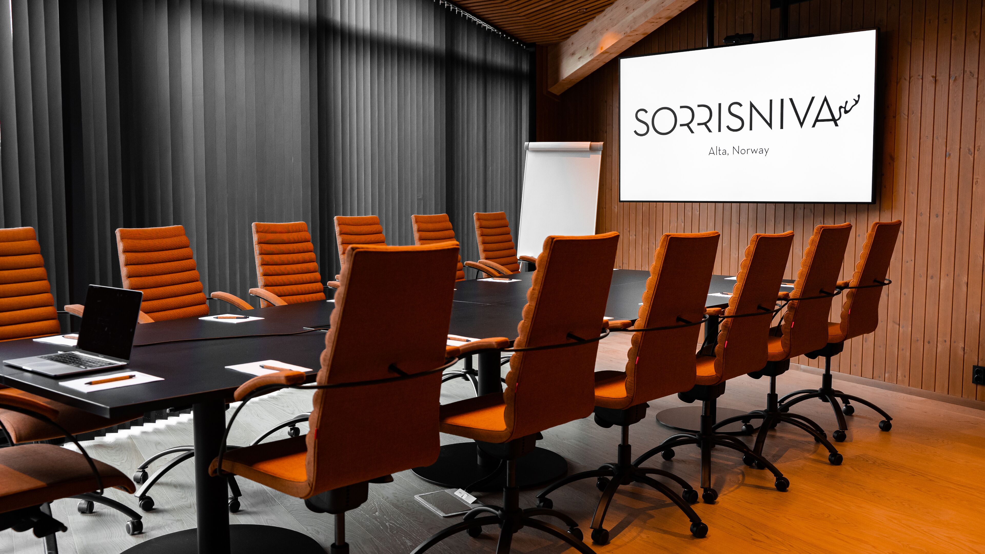 A conference room with a long table, multiple chairs, a laptop, and a presentation screen.