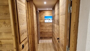 A narrow hallway with wooden walls and a wooden floor, leading to a room with a picture of a snowy landscape.