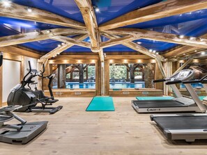 Une salle de sport équipée de tapis de course, d’un appareil elliptique et d’une piscine visible à travers de grandes fenêtres.
