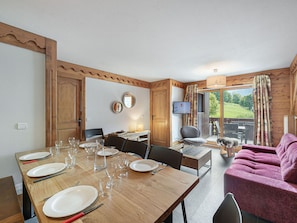 A dining area with a wooden table set for four, a sofa, and a TV in the background. - Ski-in/ski-out apartment with terrace and pool access (Méribel)