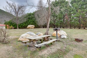 Une table de pique-nique avec des bancs, de gros rochers et une mangeoire à oiseaux, le tout situé dans une zone herbeuse, avec des arbres et des montagnes en arrière-plan.