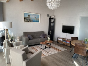 Un salon moderne comprenant un canapé, des fauteuils, une table basse, un téléviseur et une bibliothèque.