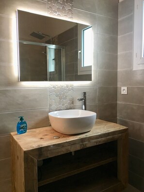 Ein Badezimmer mit einem Holzwaschtisch, einem weißen Haubenwaschbecken, einem Spiegel und einer Duschkabine.