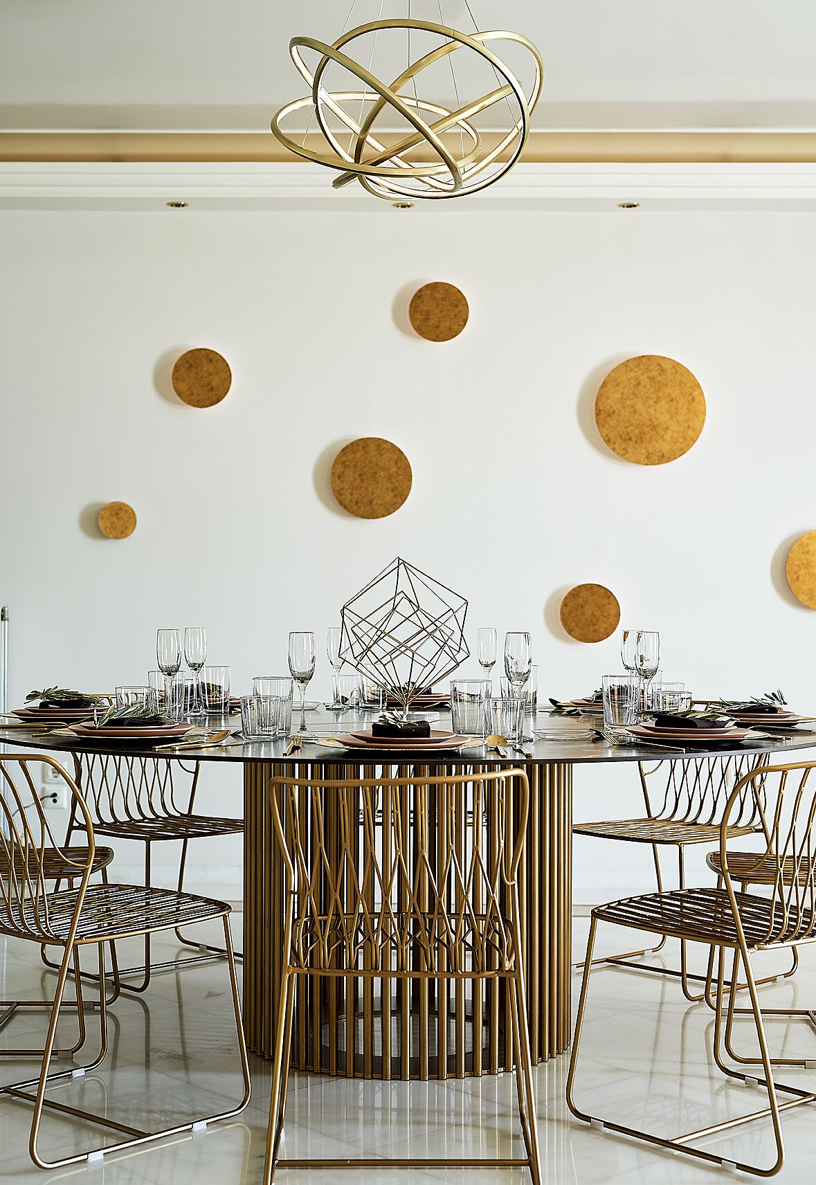 Un espace de salle à manger moderne avec une table ronde, des chaises dorées et un luminaire aux motifs géométriques.