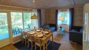 A cozy cabin interior with a dining area, sofa, and a small table with a lamp.
