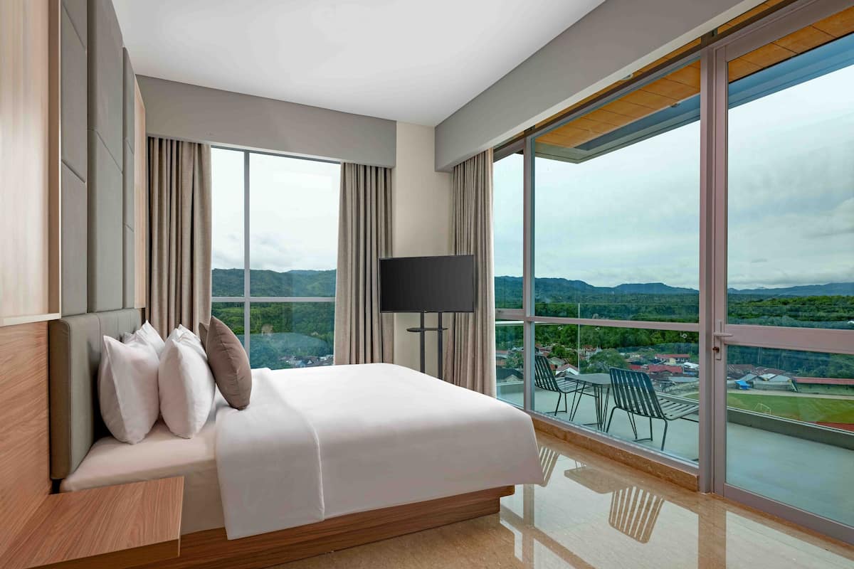 A modern hotel room with a large bed, a flat-screen TV, and a balcony with a city view.