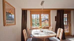 A dining area with a round table set for four, wooden chairs, a vase with flowers, and a framed picture on the wall. - Haus Lizi - Apartment 8 (Zermatt)