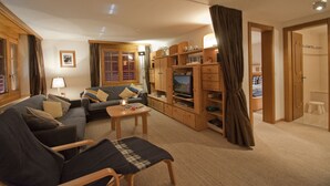 A cozy living room with a sofa, a coffee table, and a TV stand. There is a wooden cabinet with shelves and a door leading to another room. - Haus Lizi - Apartment 8 (Zermatt)