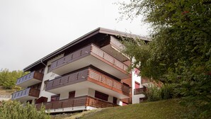 A multi-story building with balconies, surrounded by greenery and trees. - Haus Lizi - Apartment 8 (Zermatt)