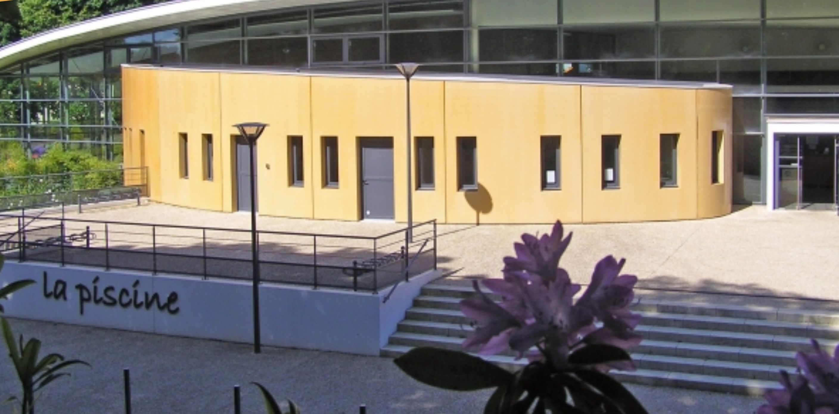 A modern building with a curved facade, a sign reading "la piscine," and a staircase leading to the entrance.