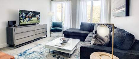 Un salon moderne avec un canapé gris, une table basse et un téléviseur posé sur un meuble.