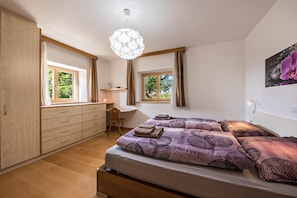 Un dormitorio con cama, escritorio y silla. Hay ventanas con cortinas, una lámpara de techo y una luz en la pared.