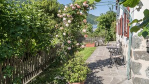 A stone pathway leading to a wooden fence with climbing roses, a potted plant, and a table with chairs. - Spacious Apartment “Lafreid Algund” near Merano with Mountain View, Wi-Fi & Garden (Algund)