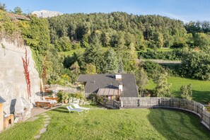 A house with a sloped roof, a fenced yard, and a view of a forested hill. - Apartment “Schlern” in Scenic Landscape with Mountain View & Garden (Völs am Schlern)