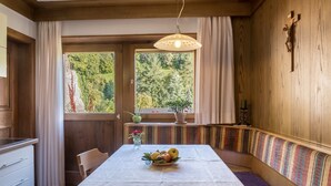 A dining area with a table, bench seating, a potted plant, and a view of greenery outside.