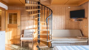 Un interno in legno con una scala a chiocciola, un divano, una poltrona fantasia e un televisore.