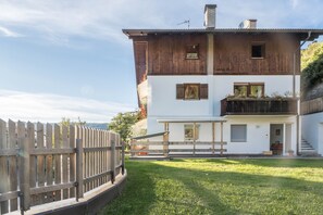 Ein zweistöckiges Haus mit Holzfassade, einem Balkon und einem umzäunten Garten.