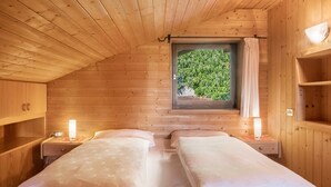 Una camera in una baita di legno con due letti, una finestra con tenda e una mensola.