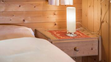 A wooden cabin interior with a bed, a nightstand with a lamp, and a wooden wall.
