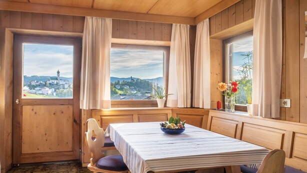 Un interno in legno con un tavolo da pranzo, sedie e vista su una città attraverso ampie finestre.